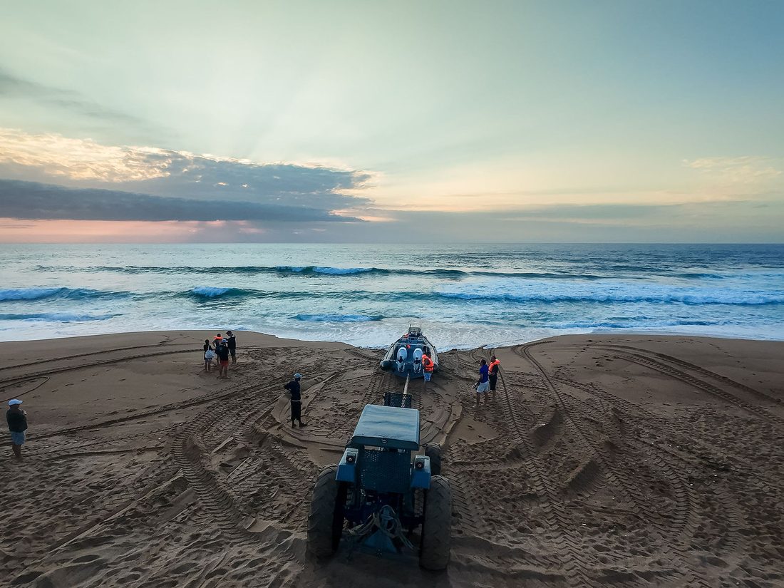 A tractor recovers a boat up the beach at Westbrook as the sun rises over the surf
