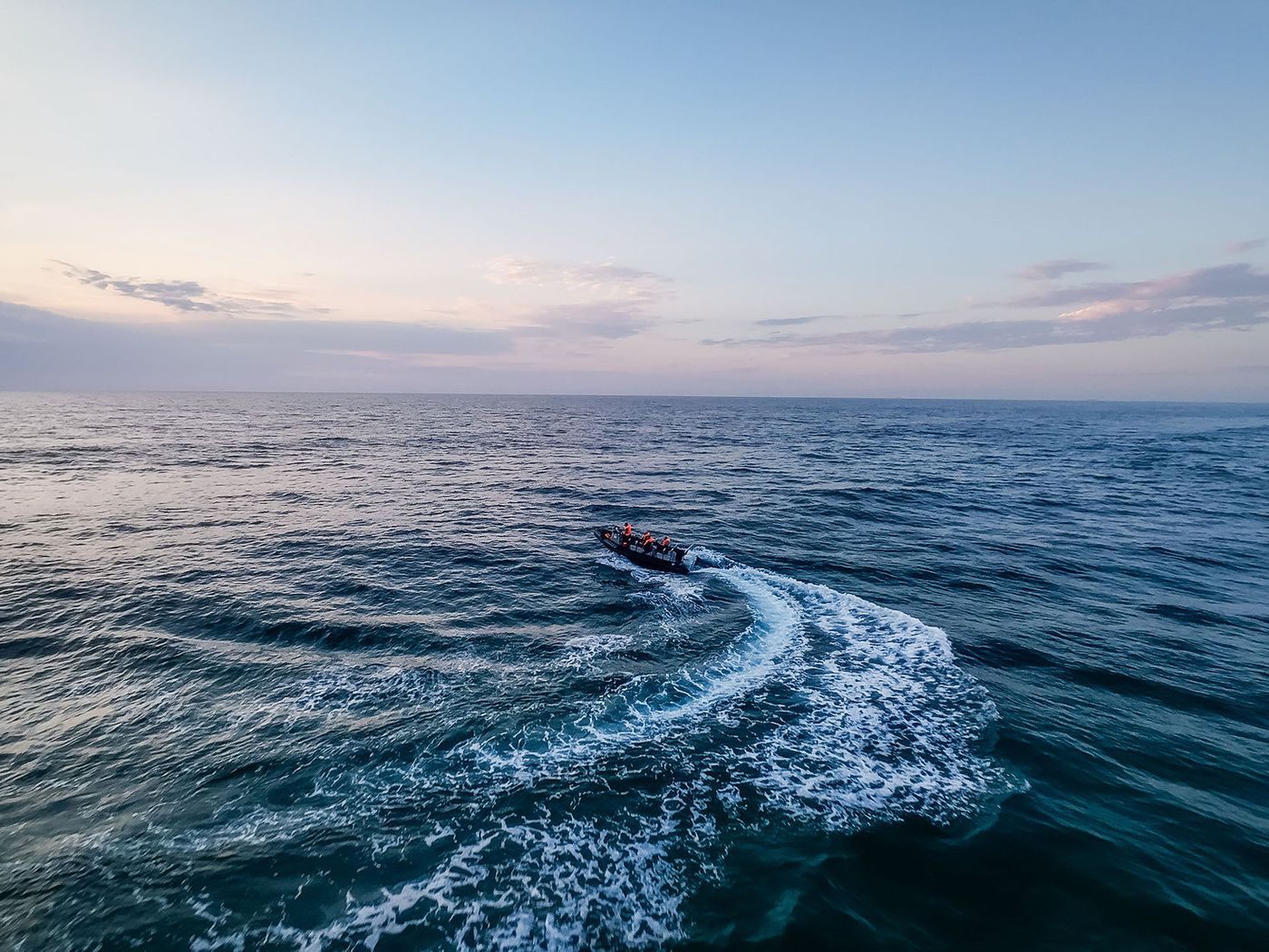 Aerial view of a rigid inflatable boat carving a curved wake across the ocean at sunrise