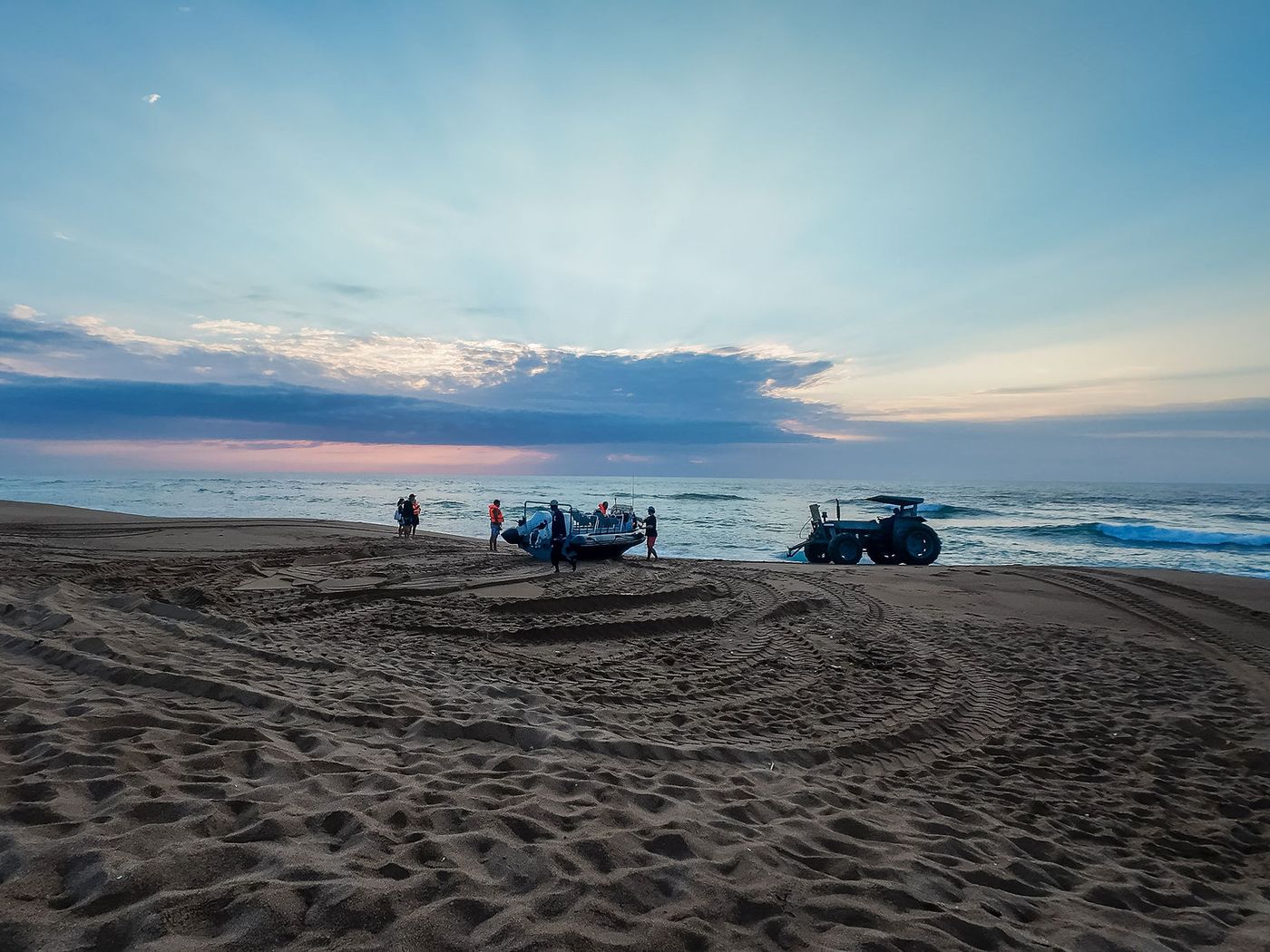 Crew, tractor and boat on the beach at first light with tractor tracks curving through the sand