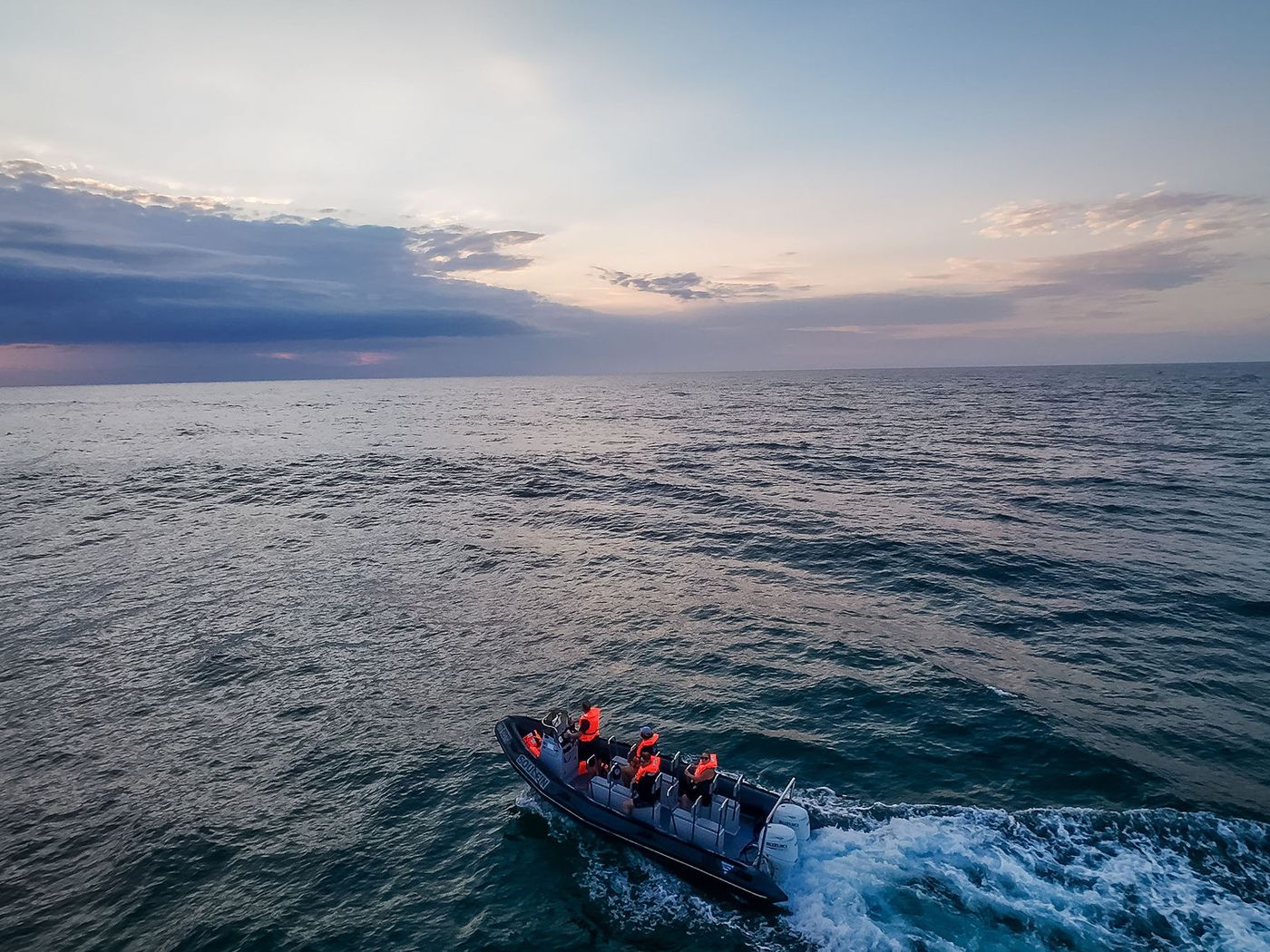 Aerial view of a crew in orange life jackets aboard a rigid inflatable boat on calm dawn water