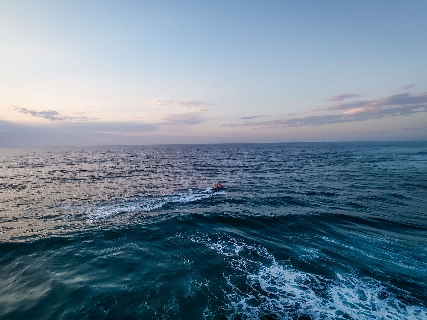 A small boat far out on open ocean under a wide sunrise sky