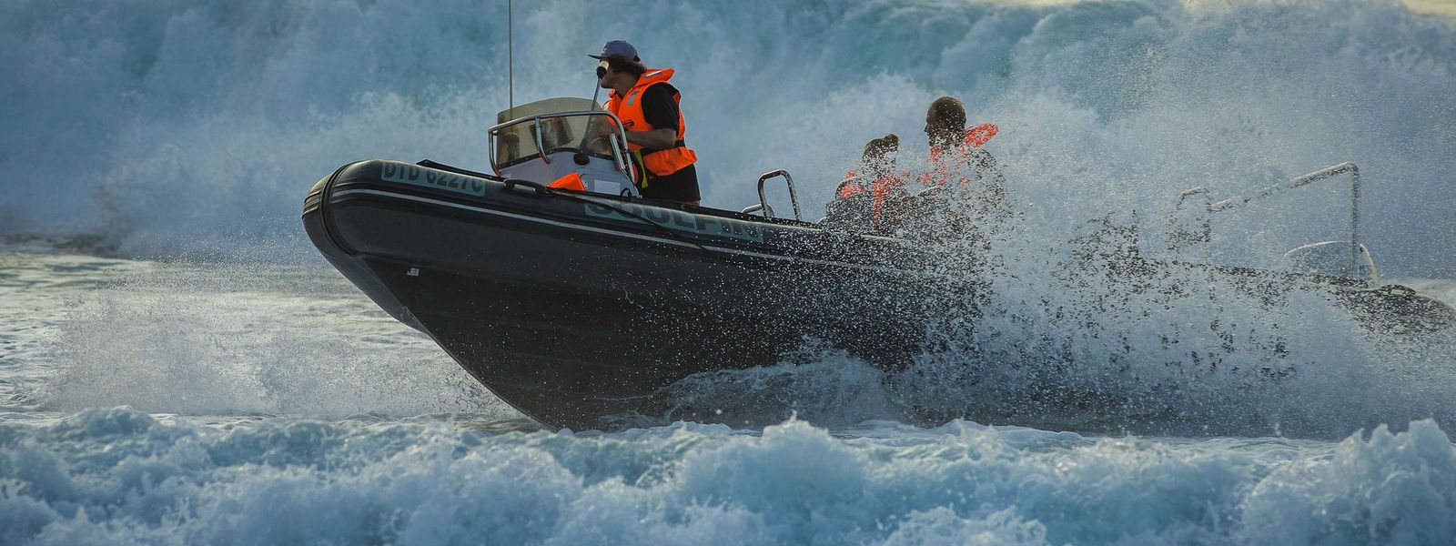 A rigid inflatable boat launching through breaking surf with the skipper standing at the helm