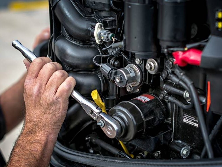 A technician working on an outboard engine with a ratchet spanner
