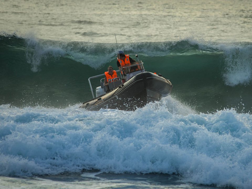 A skipper at the helm guiding a rigid inflatable boat over a breaking wave