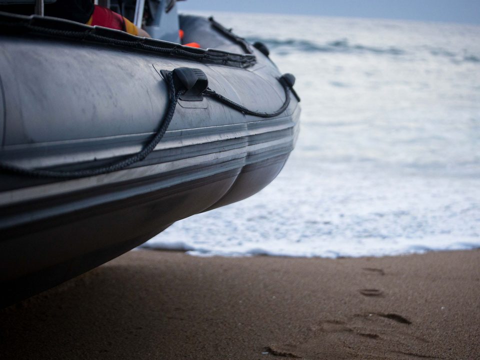 The salt-streaked pontoon of a rigid inflatable boat resting on the sand at the water's edge